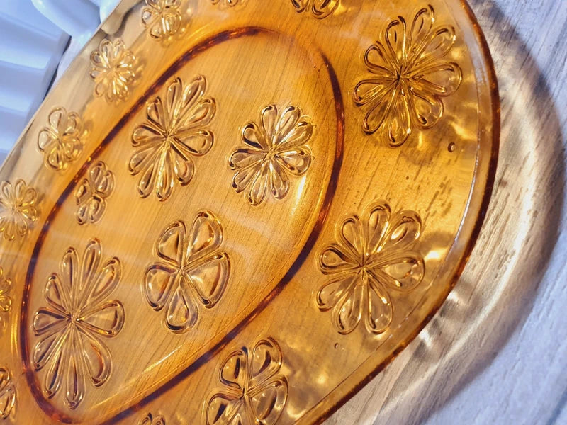 Grand plat de service de forme ovale en verre trempé épais couleur ambre transparent, orné d'un motif de fleurs marguerites moulé en relief sur le dessous, marque Vereco France époque années 1970.