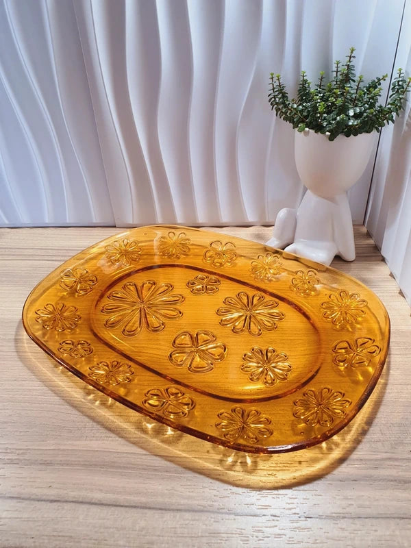 Grand plat de service de forme ovale en verre trempé épais couleur ambre transparent, orné d'un motif de fleurs marguerites moulé en relief sur le dessous, marque Vereco France époque années 1970.