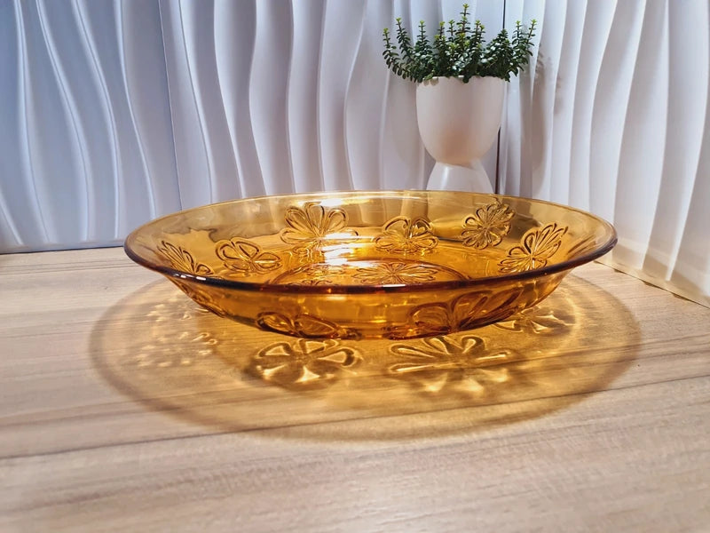Grand plat rond creux à salade en verre trempé épais couleur ambre transparent, orné d'un motif de fleurs marguerites moulé en relief sur le dessous, de la marque Vereco France époque années 1970.