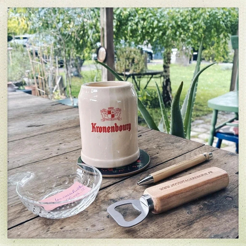 Chope à bière ancienne de marque Kronenbourg en céramique émaillée couleur crème et rouge en forme de tonneau publicitaire, inscription Baudour Belgium CRF sous le dessous, style bistrot vintage des années 1970 utilisé comme cache-pot décoratif pour plante verte.