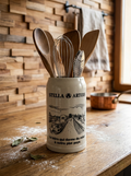 Grande choppe à bière en grès beige portant le logo Stella Artois et l'inscription noire "la bière qui donne du relief à notre plat pays" avec une illustration de péniche. Détourné pour ranger des ustensiles de cuisine.