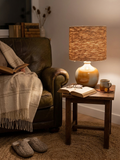 Une lampe vintage imposante composée d'un pied en grès français beige moucheté et d'un grand abat-jour en toile de jute tressée, diffusant une lumière chaude dans un intérieur à la décoration naturelle.