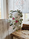 Pot mural arrondi en porcelaine blanche brillante orné de motifs de roses roses et rouges, avec trous de fixation au dos, style vintage romantique. Utilisé en cache pot avec une magnifique plante tombante style chaine de coeur. 