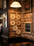 Une décoration murale de style brasserie vintage. Sur un mur en briques rouges apparentes, six sous-bocks ronds en bois clair avec le logo "Leffe" sont fixés de manière décorative. L'ensemble est entouré d'éléments typiques de pub